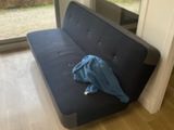 a couch with a blue shirt on it in front of a window