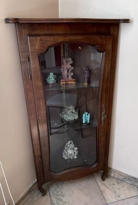 une armoire d'angle avec une porte vitrée, placée dans un coin de la pièce
