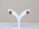 une paire de boucles d'oreilles ornées de pierres orange, posée sur un support blanc sur une table