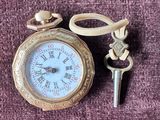 une petite montre de poche en or et une clé posées sur un tissu violet