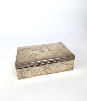 une vieille boîte en argent portant une inscription, posée sur une surface blanche