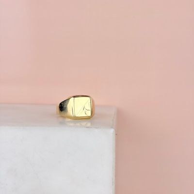 un gros plan d'une bague chevalière en or posée sur un bloc de marbre