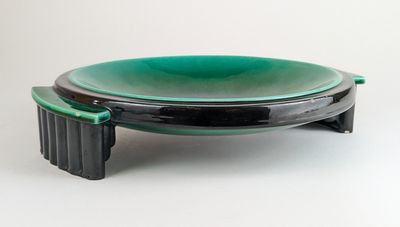 une assiette verte et noire posée sur un support, sur une surface blanche