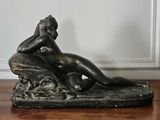 bronze statue of a woman sitting on a rock on a wooden table
