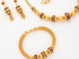 a gold necklace, bracelet and earring set with red and green beads