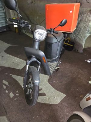 un scooter garé dans un garage, avec un carton à l'arrière