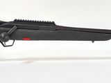 un fusil noir posé sur un socle transparent, sur une surface blanche