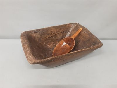 un vieux bol en bois posé sur une table, avec une cuillère à l'intérieur