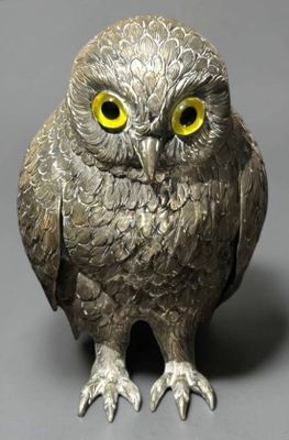 figurine de chouette argentée aux yeux jaunes, posée sur une surface grise