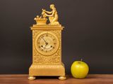a gold clock and an apple on a wooden table