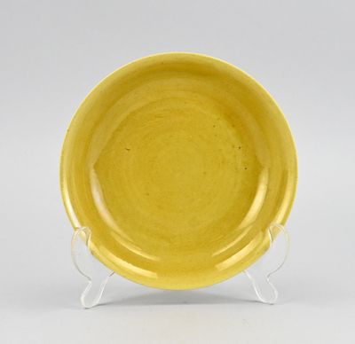 une assiette jaune posée sur un support, sur une surface blanche