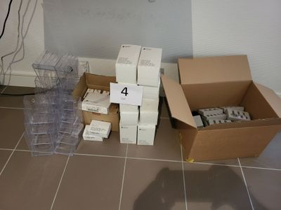 plusieurs cartons contenant du matériel électronique posés sur un sol carrelé, près d'un mur