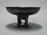 a black bowl on a stand on a white surface