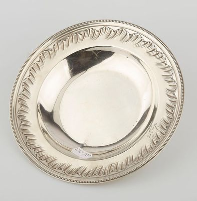 an antique silver plate on a white surface with a black feather on it