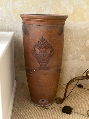 un grand vase marron posé par terre près d'un mur