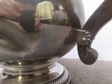 une théière en argent posée sur une table, avec une personne en arrière-plan