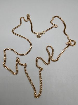 gros plan d'un collier en or avec une chaîne sur une surface blanche