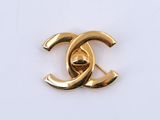 un gros plan d'une broche Chanel plaquée or sur une surface blanche
