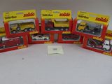 six camions miniatures assortis, emballés dans leurs boîtes, posés sur une surface blanche