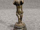 une statue en bronze représentant un garçon tenant un ballon, posée sur un socle