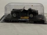 a black toy car in a clear box on a white surface