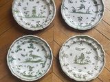 four plates with green and white designs on them sitting on a wooden floor