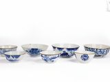 six bols en porcelaine bleue et blanche et un bol posé sur une surface blanche