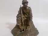 statue représentant un homme assis sur un rocher, un fusil à la main