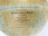 un petit globe posé sur un socle en bois, lui-même posé sur une surface blanche