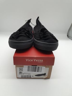 des Vans noires sans lacets posées sur une boîte rouge, sur une surface blanche