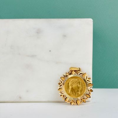 broche plaquée or à motif « sunburst » posée sur une surface en marbre blanc