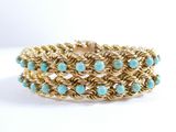 a close up of a gold and turquoise bracelet on a white background