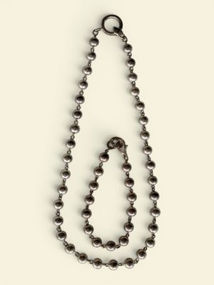 a close up of a metal beaded necklace on a white surface