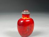 a red glass vase with a silver lid on a white surface