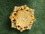 une photo d'une broche en or et diamants posée sur un tissu vert