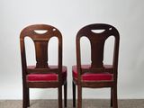 two wooden chairs with red upholstered seats against a white wall