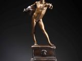 a bronze statue of a boy holding a football ball on a red pedestal