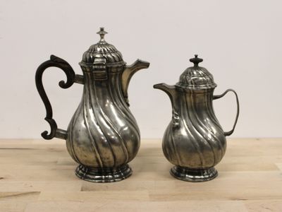 une paire de cafetières anciennes en métal argenté posées sur une table en bois