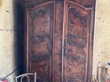 a wooden armoire in the corner of a room with a chair and a stool