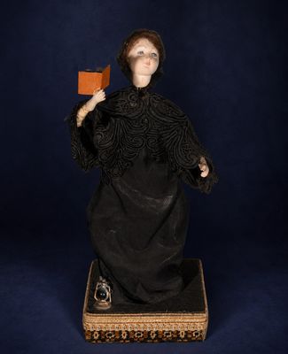 an old fashioned doll with a black dress and a red hat