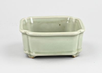 un petit pot vert muni d'une anse, posé sur une surface blanche