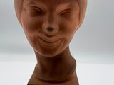 une sculpture en argile représentant la tête d'une femme, posée sur un socle en bois