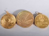 three gold medallions of different sizes and shapes on a white surface