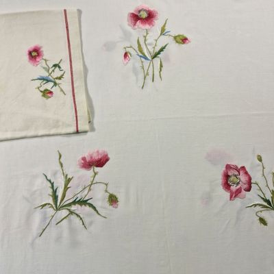 embroidered tablecloths with pink flowers and green stems on a white table