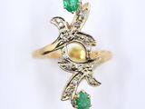 a close up of a gold ring with a pearl and emerald stones