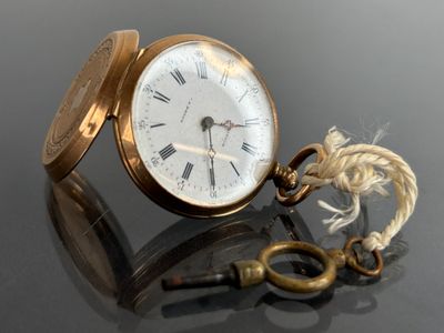 a gold pocket watch with a key on a table