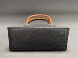 an old black suitcase with a wooden handle sitting on a gray surface