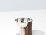 un petit bol en métal reposant sur un socle en bois, posé sur une surface blanche