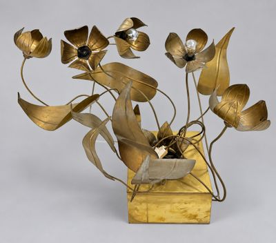 brass flowers in a vase on a wooden stand with a white background
