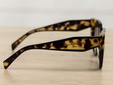 leopard print sunglasses on a wooden table with a white wall in the background